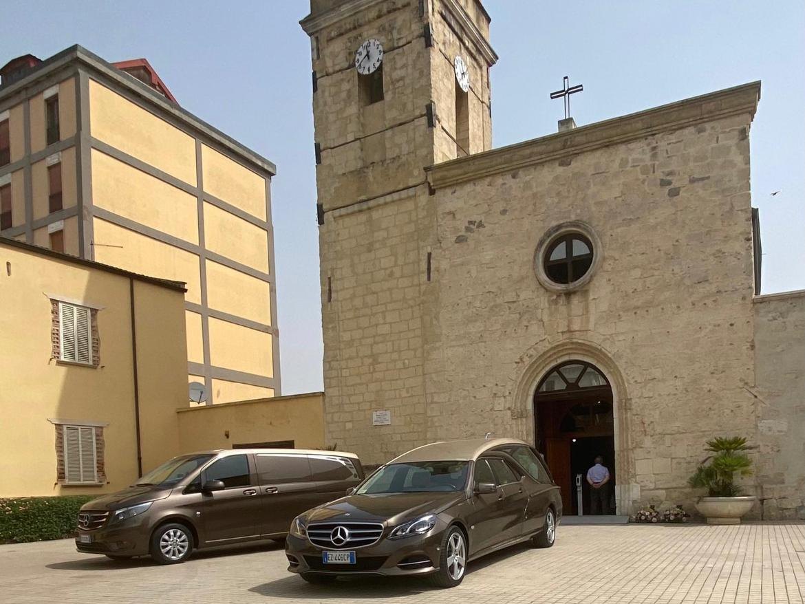 Carro funebre e vettura di servizio davanti alla chiesa durante un funerale ad Assemini